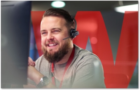 Bearded person in a headset smiling and looking at a computer monitor